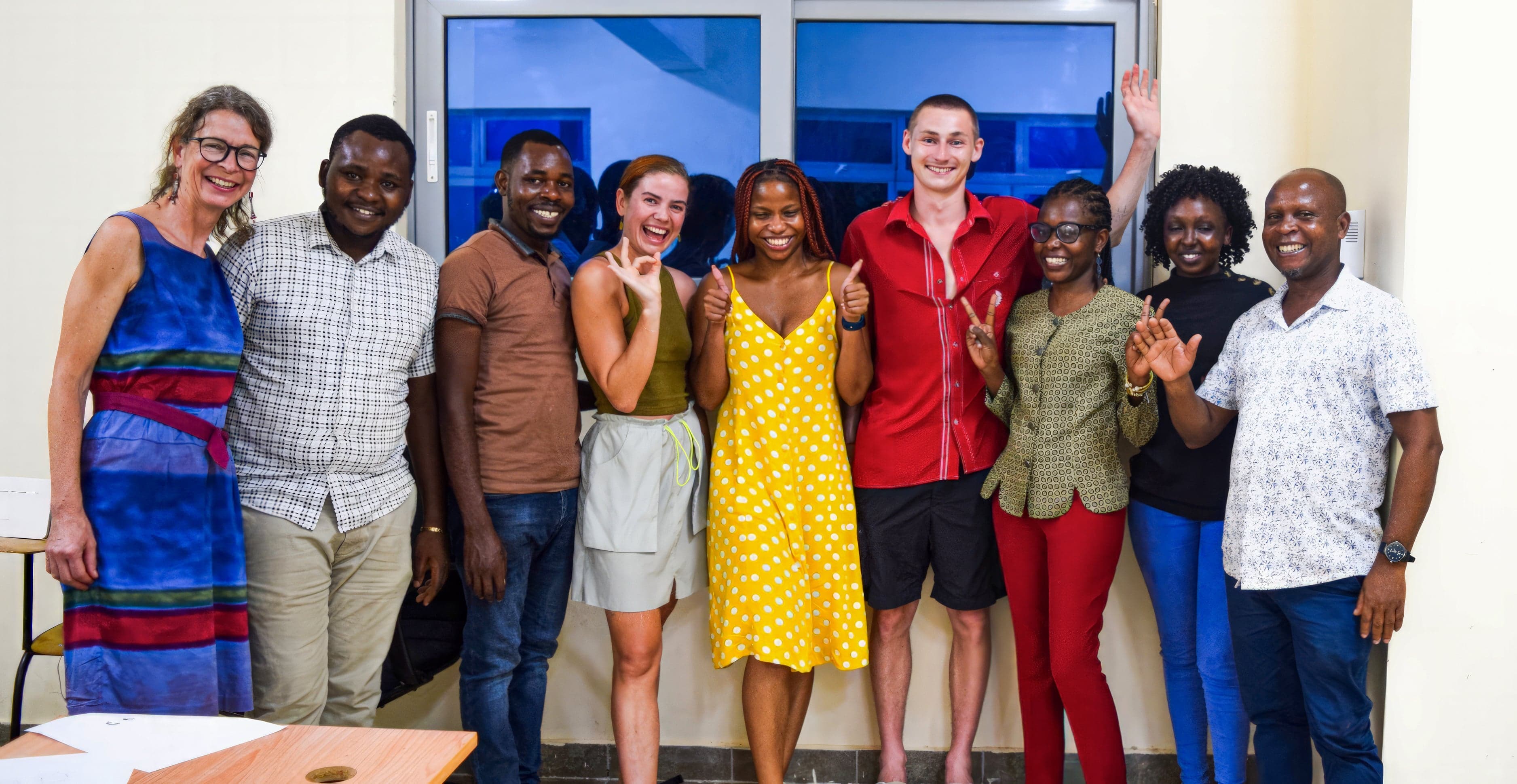 Olivia and Lukas posing with seven students outside Pwani University, Kilifi, Kenya" Caption: "Olivia and Lukas with students from our graphic design workshop at Pwani University,