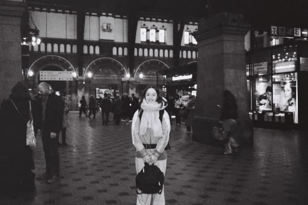 Black and white image of a young designer standing in the middle of Copenhagen Central Station, wearing a backpack and ready to start a digital detox journey