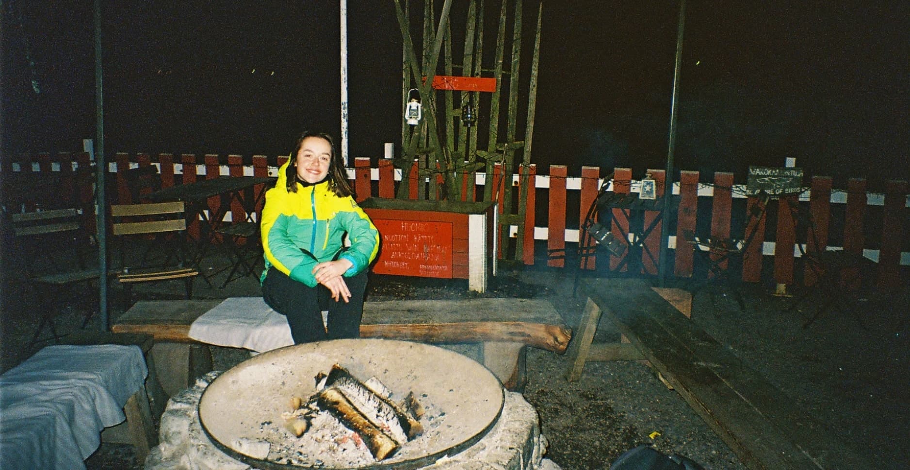 Designer sitting alone on a bench by a bonfire in Helsinki at night, reflecting during a digital detox journey.