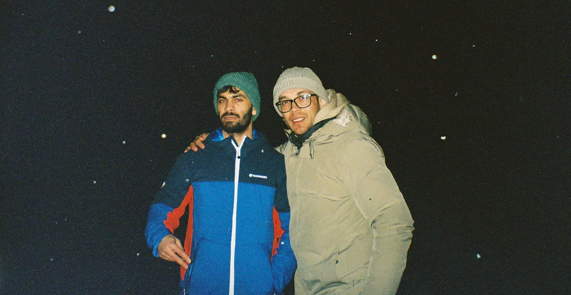 Nighttime photo of two Iranian friends met during a digital detox trip, standing in the middle of a frozen lake in Finland.